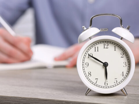 alarm clock in foreground, person writing in background