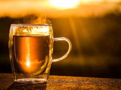 cup of black tea in a glass cup against a sunset